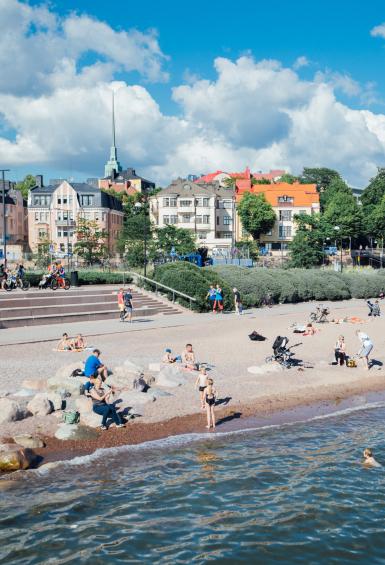 With the houses and apartments of Eira in the background against a blue sky, dozens of people lay scattered across Eiranranta beach, the sea lapping on the shore. 