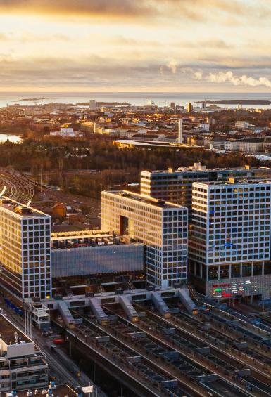 A panoramic, aerial view of a sunset over Pasila neighbourhood, picturing the Mall of Tripla and the train station. 
