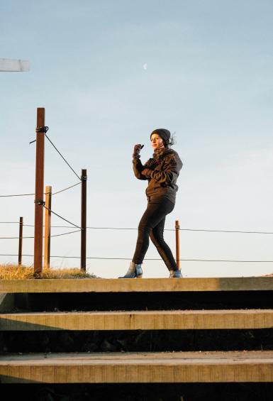 Looking up towards her, Priyanka Banerjee stands at a plateau on top of some wooden steps, in the midst of practicing martial arts, blue sky behind her.
