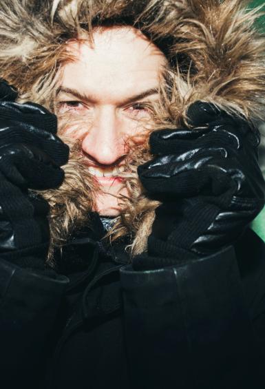 Portrait of Olivier Béaslas from the shoulders up, pulling a fur lined coat hood over most of his face while smiling.
