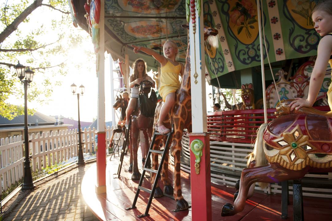 3 girls riding the merry-go-round at Linnanmäki amusement park, one girl pointing excitedly to something out of sight on the left.