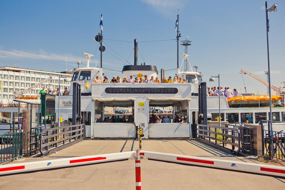 Viewed from the end of the gangway, a Suomenlinna ferry is docked at the Market Square, where passengers wait to disembark. People are waiting on deck and below deck.