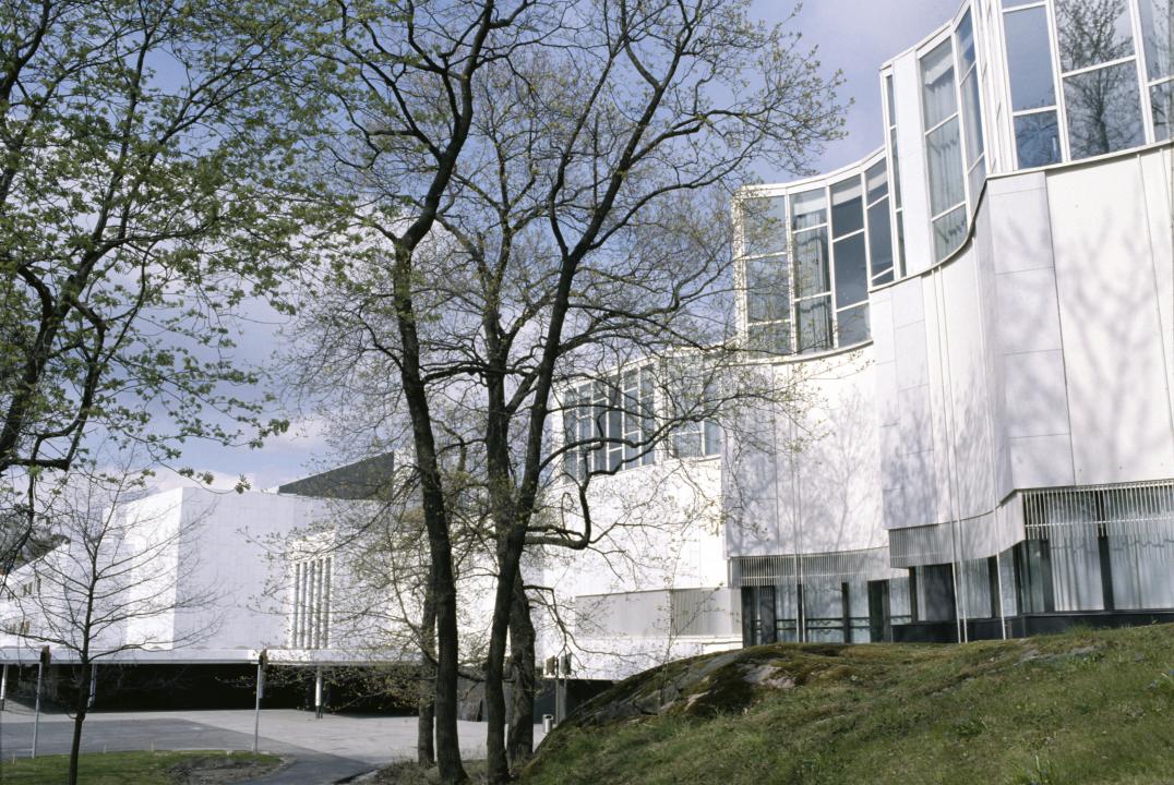 Exterior view of Finlandia-Hall's congress wing, with it's wavy architecture standing behind a pair of mostly bare trees.
