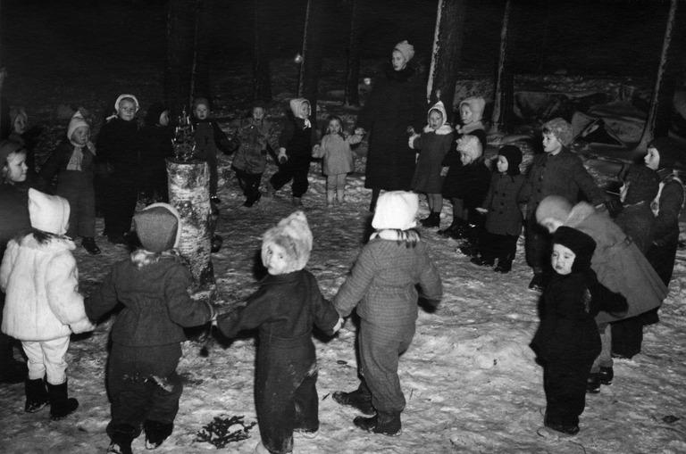 Joulujuhlat puistossa. Lapset ja nainen seisovat käsi kädessä piirissä.