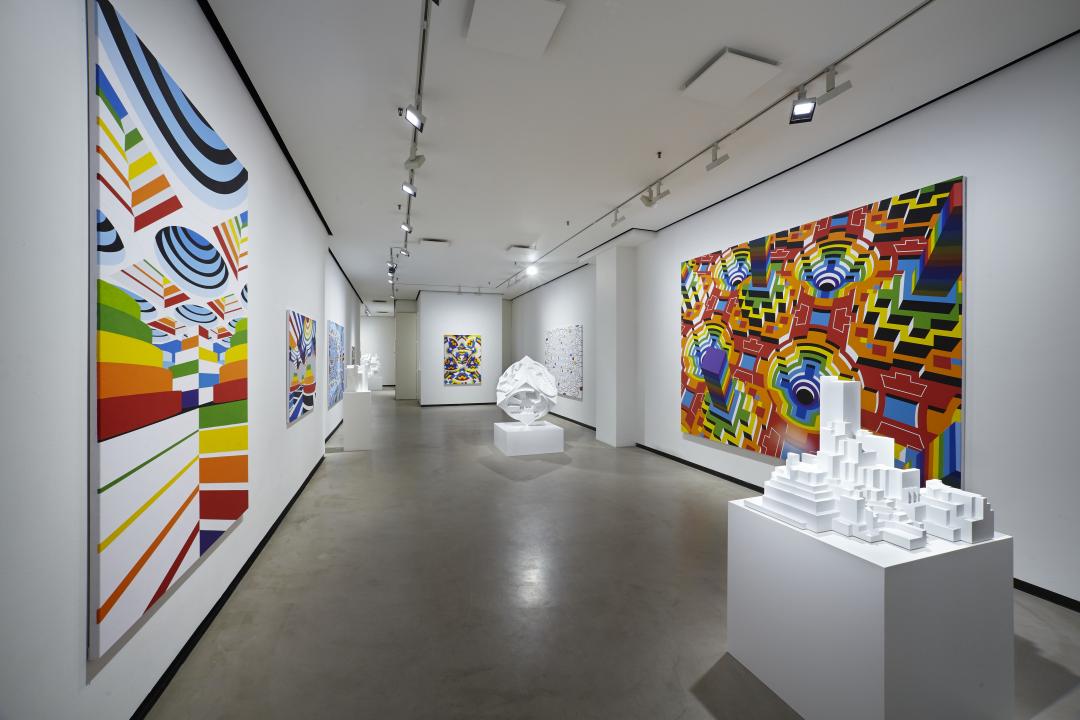 A long and wide corridor stretches ahead, on either side are large colourful paintings by Alvar Gullichsen. In the middle of the corridor are two plinths holding pure white geometrical sculptures.