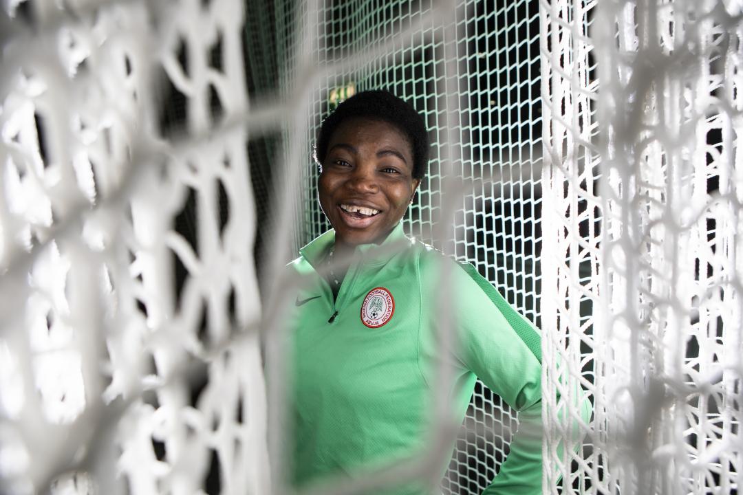 Ayisat Yusuf is smiling at the camera, standing behind sports netting.