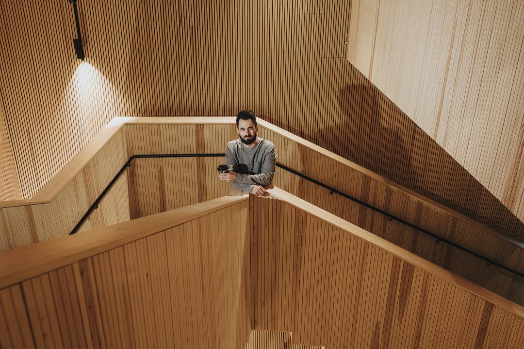 Matthew Äikäs-Adams stands in the stairwell of Helsinki University's Think Corner lookin up towards the camera. The stairwell is clad completely in wood.