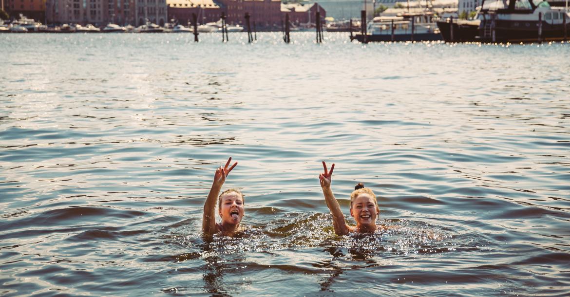 Two women swimming in Katajanokka bay on a sunny summer's day, stop to throw peace signs at the camera.