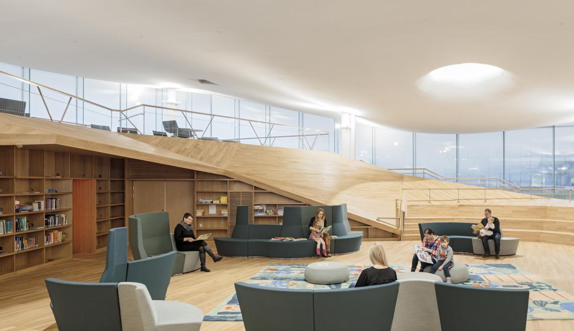 A view of the stairs sweeping up and around to the left, sofas and an open area for kids to play in the center of the space.