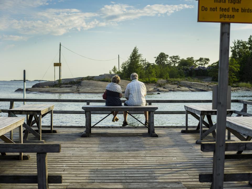 On older couple sits together on one of the cleaning benches at Merisatama's mattolaituri, facing the island and the sea in front of them. 