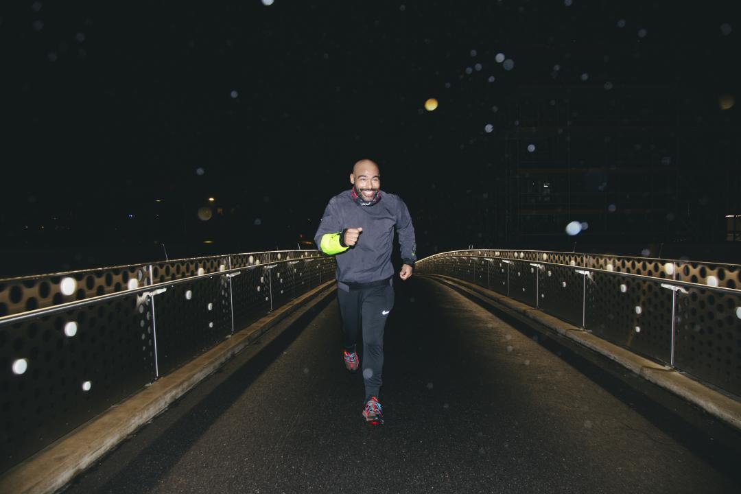Lorenzo Dotson-Smith jogging on a footbridge at night, coming towards the camera.