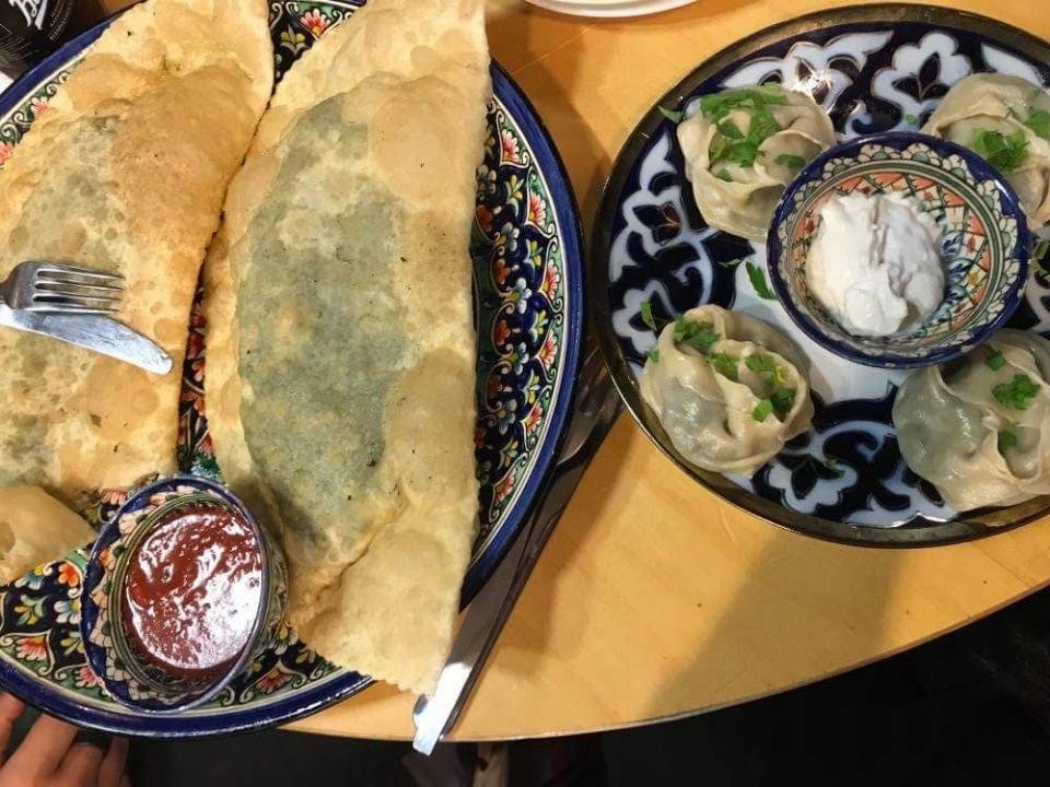 Close up of two Chebureki and dumplings with sauces served on separate plates, shot from above.