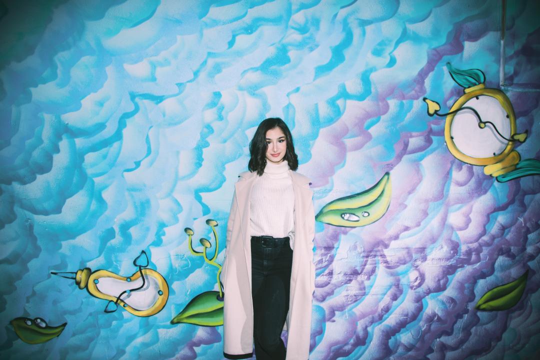 Helen Hamzaaghaei standing in front of a colourful wall mural, facing the camera.