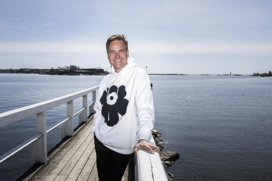 Mika Ihamuotila, facing the camera, smiling and standing on a small pier at Ullanlinnanlaituri with the sea stretching out behind him to the horizon.