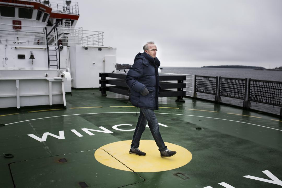 Seppo Knuuttila walking across the deck of a large ship under a grey and slightly stormy sky.