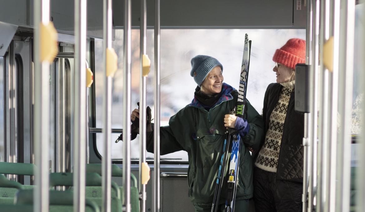 A view inside from a tram, holding poles on both sides of the image and in the background two women carrying skis with them