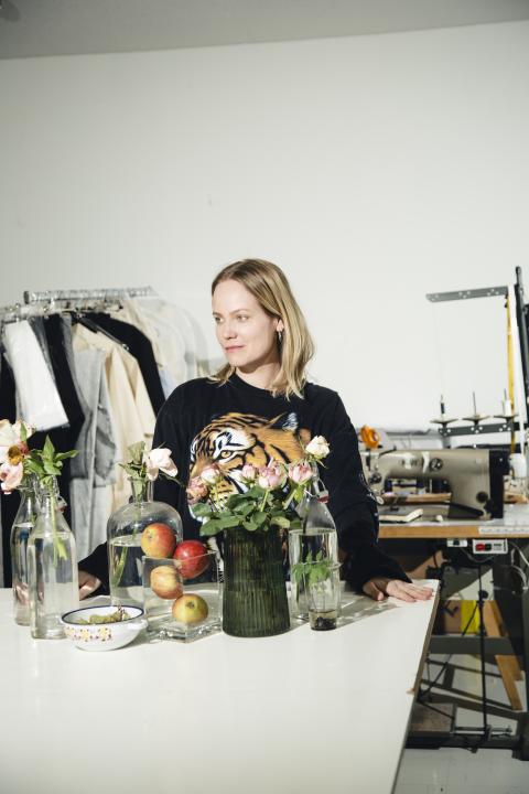 Elina Onkinen behind a table which is covered with different items, workspace in the background
