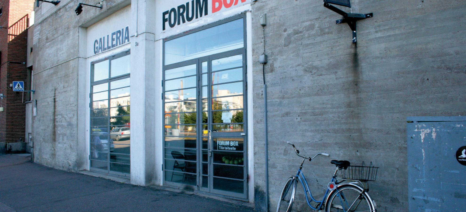 Entrance way to Forum Box art gallery, set within a grey concrete wall, bicycle leaning against the wall.