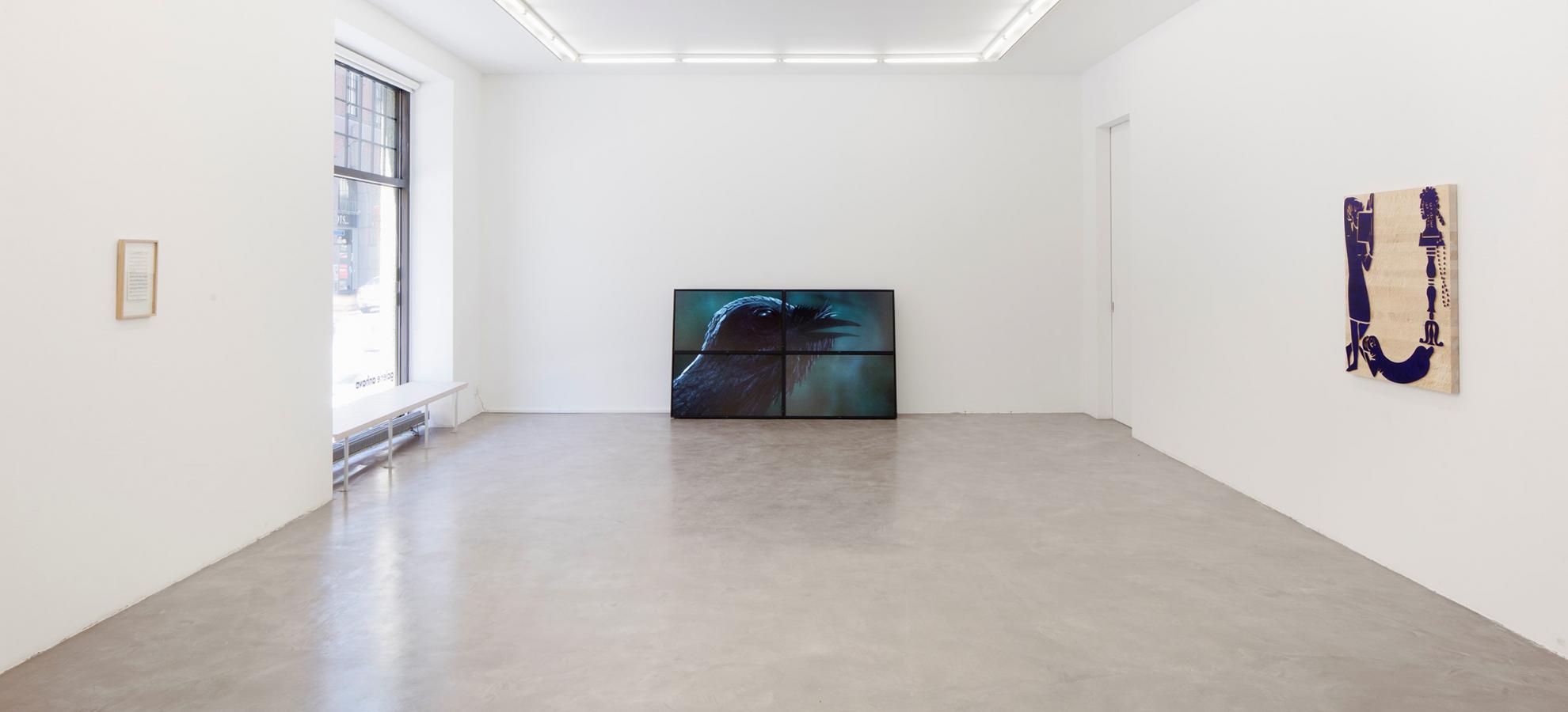 Inside a minimalist exhibition space with pure white walls and a grey floor, one painting hangs from the wall to the right, another stands on the floor directly opposite the camera.