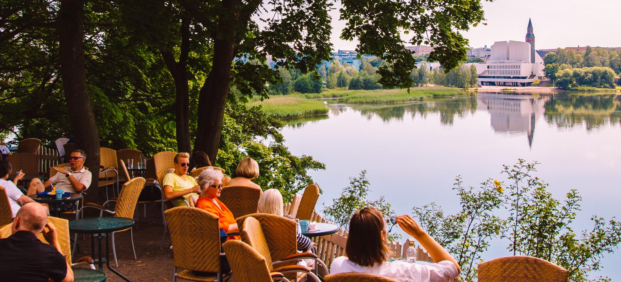 People sit and enjoy the view from Sininen Huvila summer café's outdoor terrace overlooking Töölönlahti Bay.