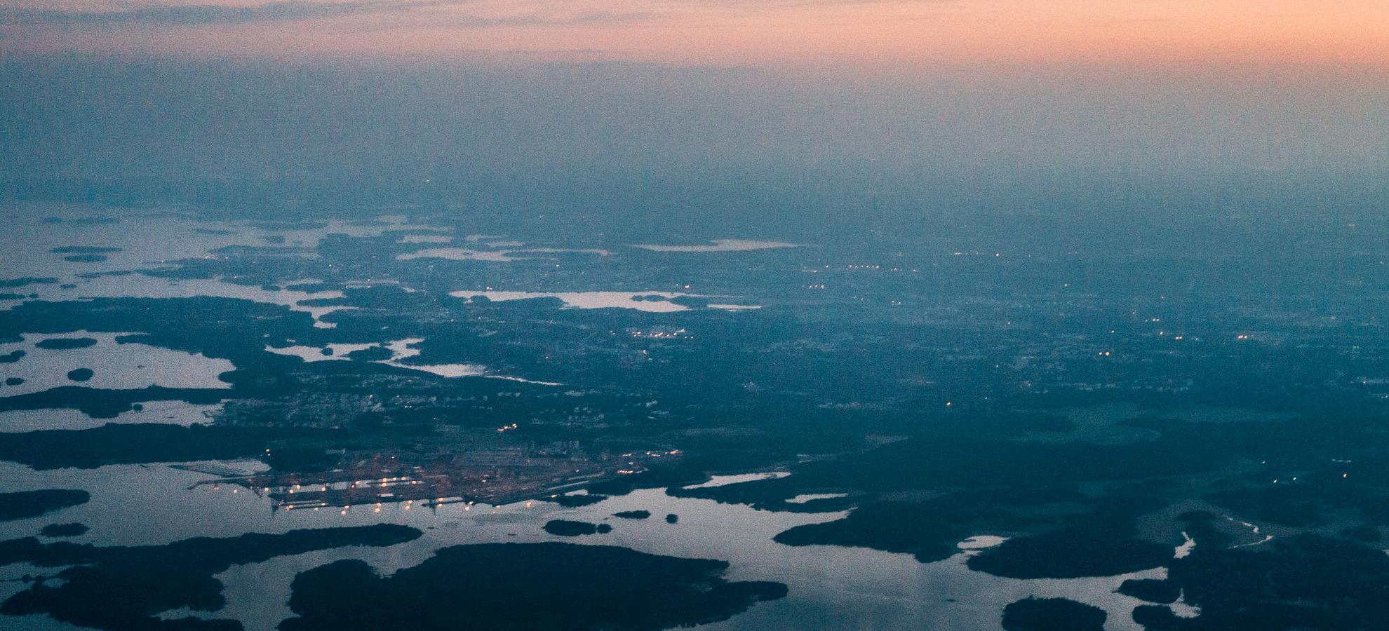 Aerial of the Vuosaari Harbour and the vast surrounding landscape at dusk. The view stretches from the islands along the coastline into the horizon kilometres away.