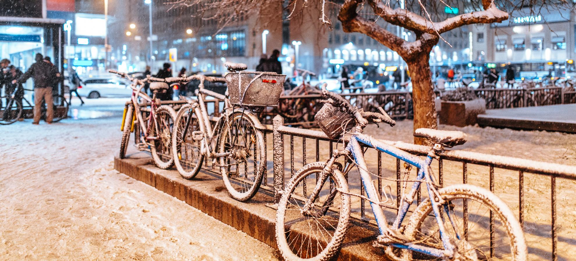 Next to the Central Railway station metro entrance on Kaivokatu, several bikes that have been locked to the railings are covered in snow.