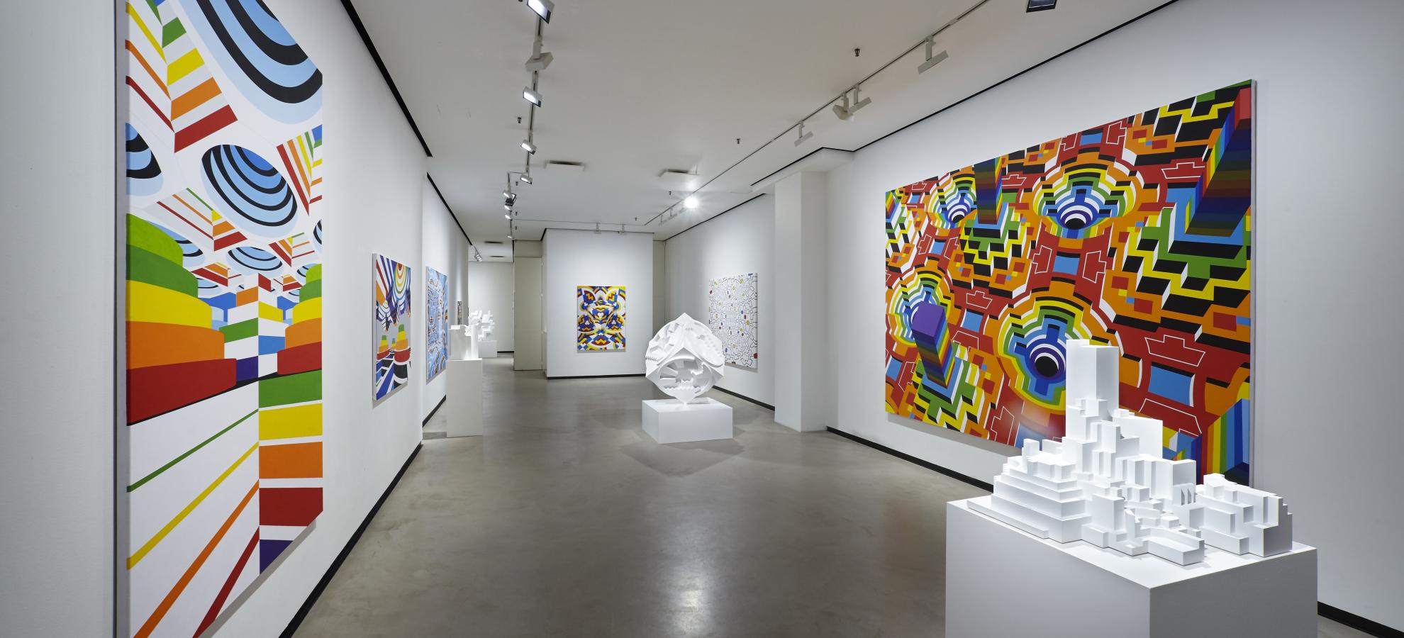A long and wide corridor stretches ahead, on either side are large colourful paintings by Alvar Gullichsen. In the middle of the corridor are two plinths holding pure white geometrical sculptures.