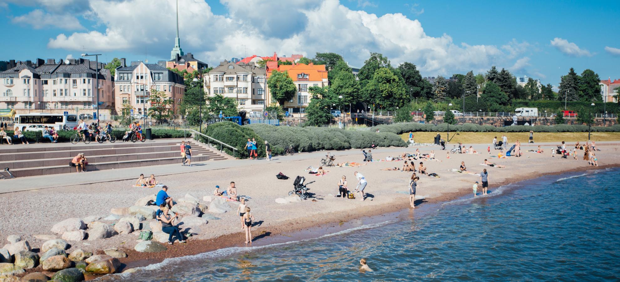 With the houses and apartments of Eira in the background against a blue sky, dozens of people lay scattered across Eiranranta beach, the sea lapping on the shore. 