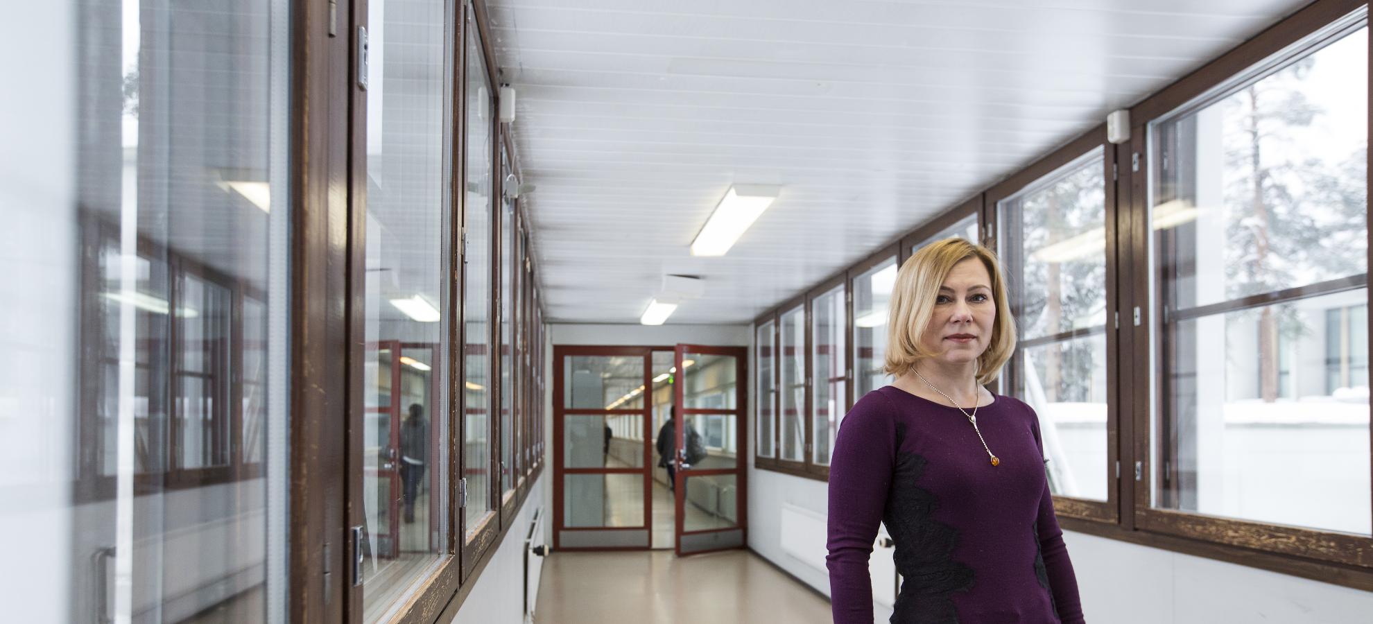 Jelena Nerman facing the camera, stands in an empty corridor lit by windows to the right of her.