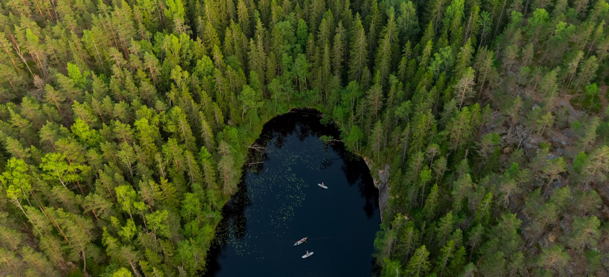 Aerial view of a small, dark lake shaped like a thumbprint, surrounded by trees in Nuuksio national park.