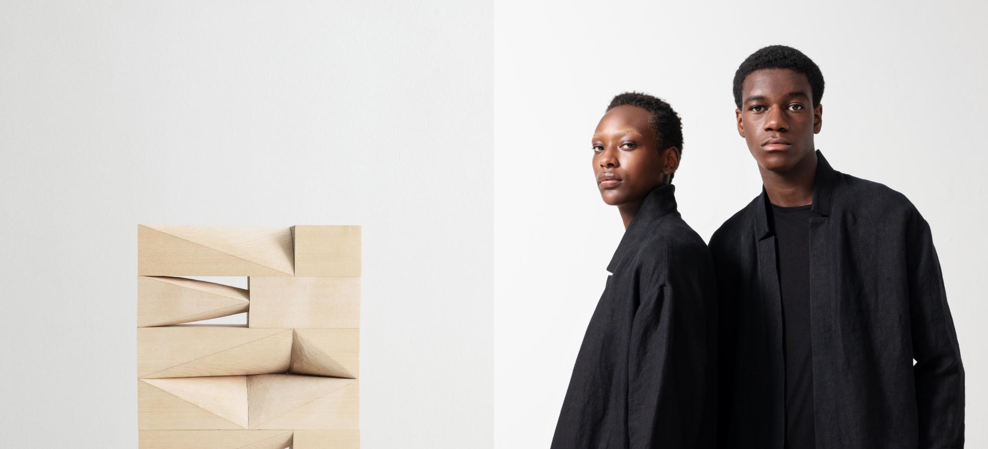 Two photos merged into one. On the left is a modern art sculpture standing on a white plinth in a gallery. On the right are two models dressed in long black clothes against a white background.