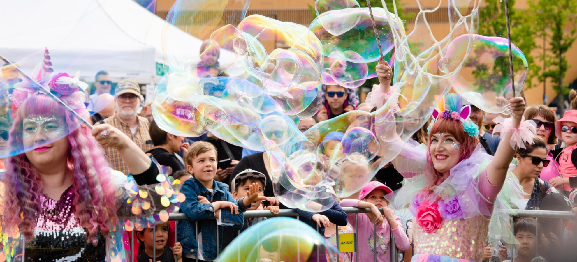 A crowd of people watching performers making giant soap bubble