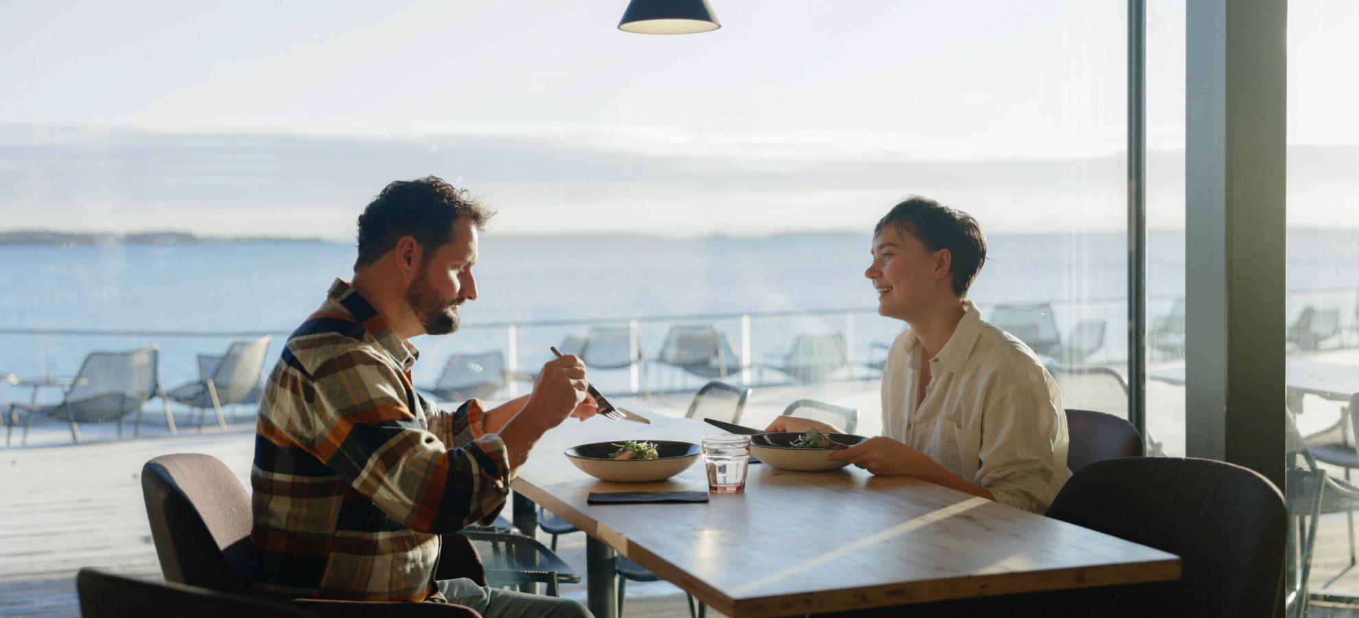 A couple eating at a table, seaview on the background